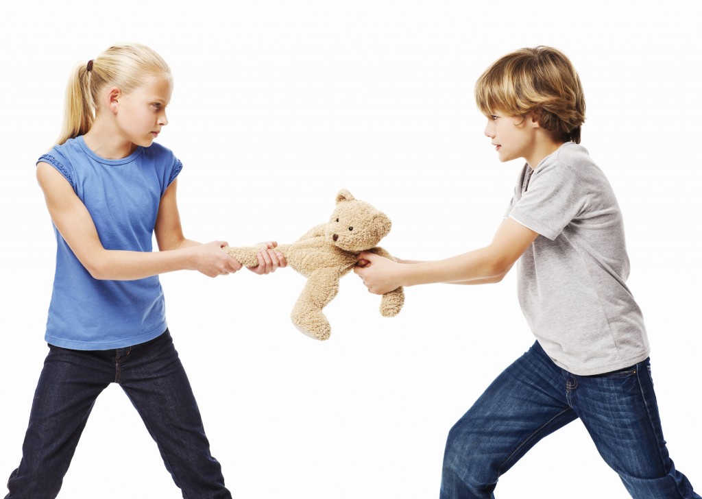 Brother and sister pull at a stuffed teddy bear. Horizontal shot. Isolated on white.