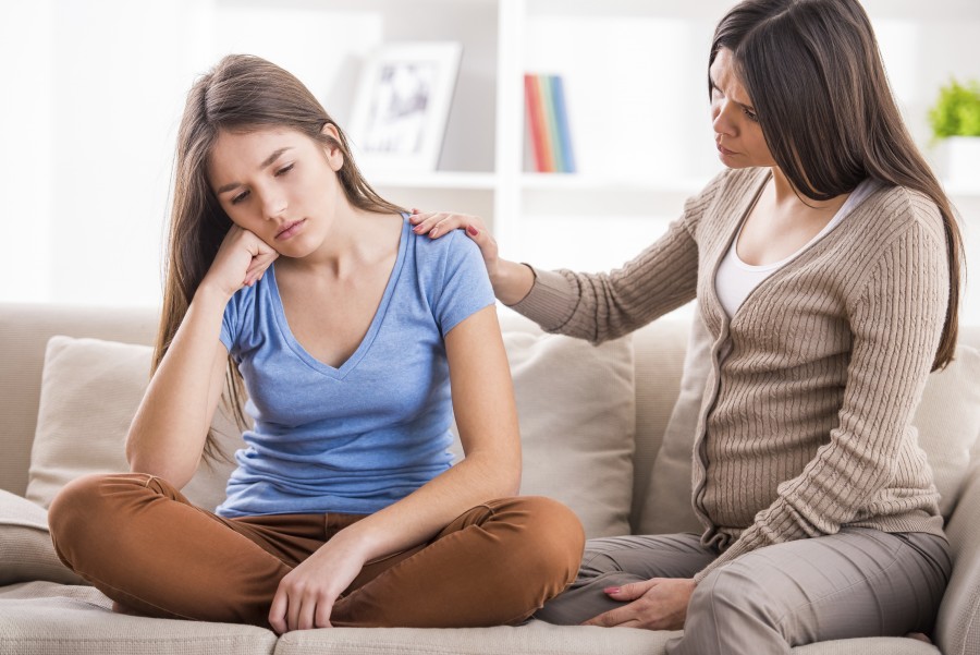 Mother and teen daughter after quarrel on sofa at home.