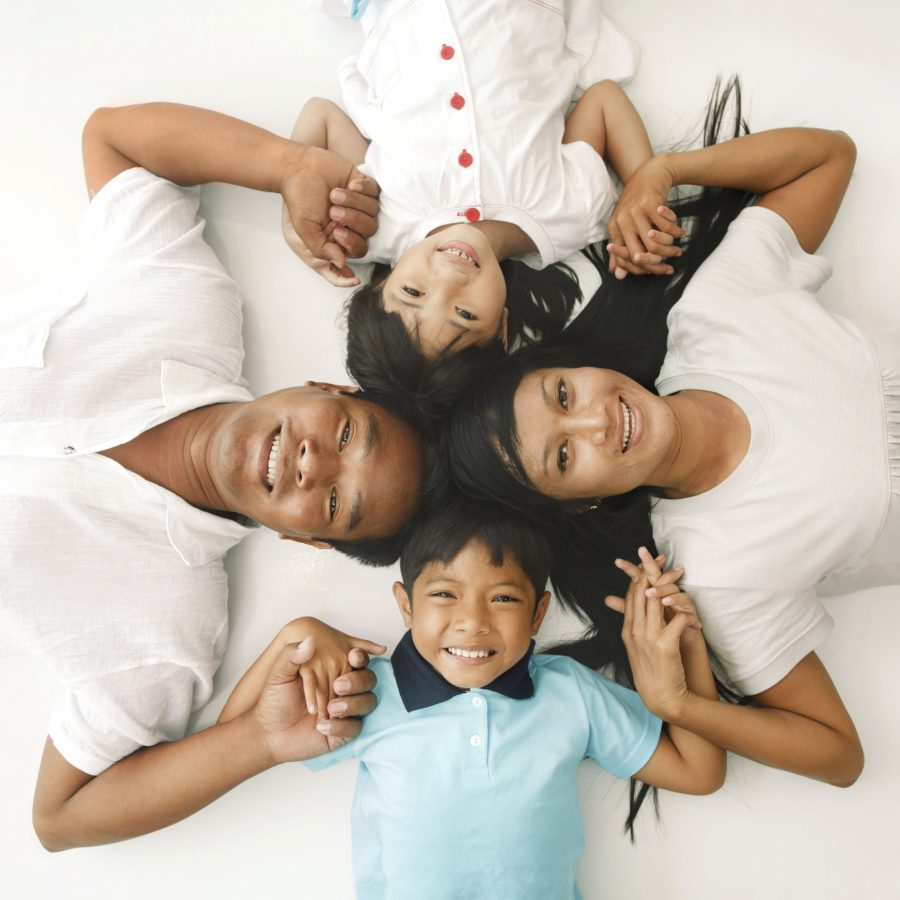 High angle view of cheerful Asian family lying down on the floor and holding hands. They are looking at camera.